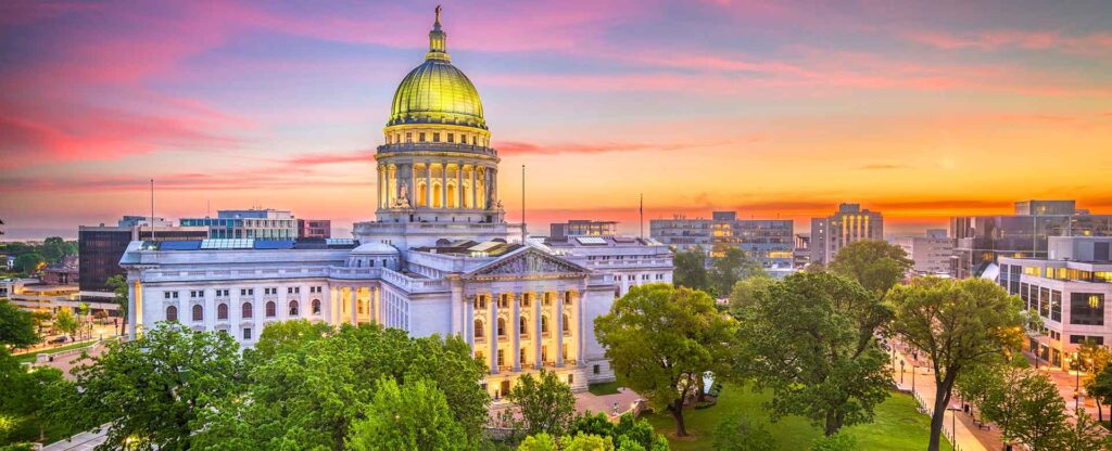 August 2025 Newsletter 2 BPI Color Madison WI view of the Wisconsin State Capitol at sunset, surrounded by lush trees and city buildings in downtown Madison.