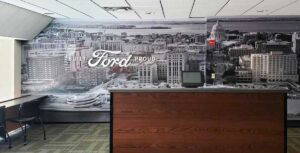 Cityscape wall mural with lettering signage "FORD", displayed behind a wooden desk.