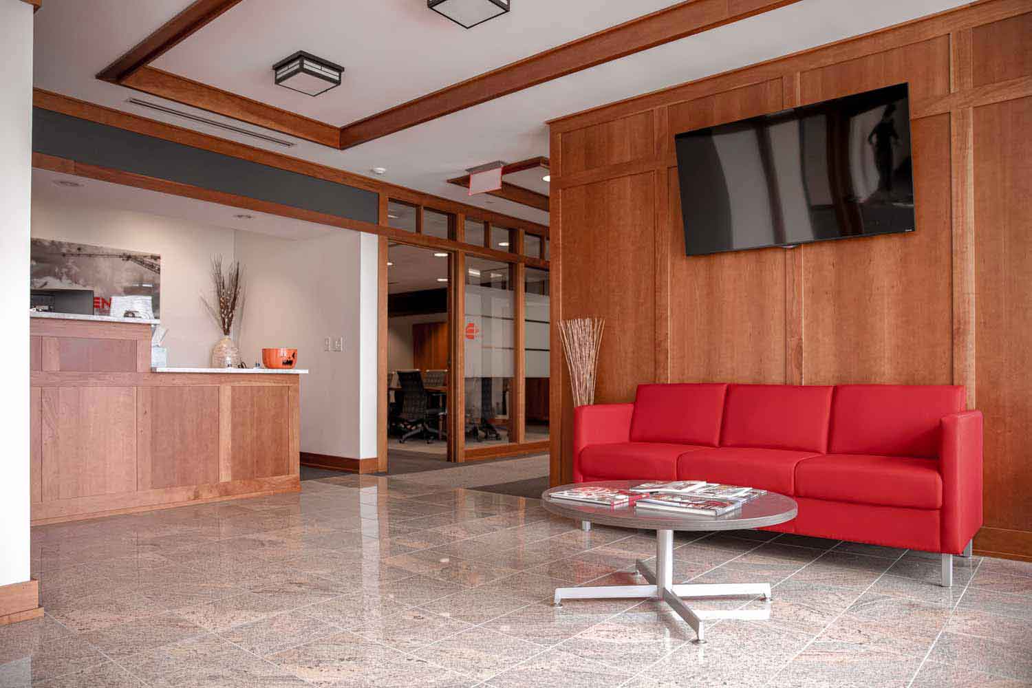 JP Cullen reception area with a large red couch sitting beneath a mounted TV and a view of the front desk.