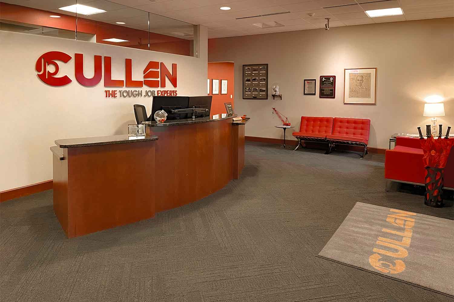 Front desk view in JP Cullen's waiting room with chairs, a rounded desk, and the JP Cullen Logo displayed on the wall.