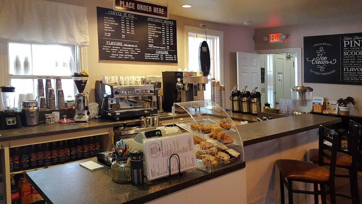 Front counter view of a coffee shop/ cafe, displaying two menu boards and a pastry cabinet.