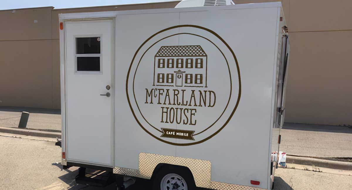 McFarland House Cafe logo on a small white food truck, parked in a parking lot.