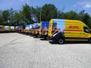 Home 98 DHL Fleet Graphics featuring a row of vibrantly wrapped delivery vans with country-themed designs, showcasing global branding and visual consistency.