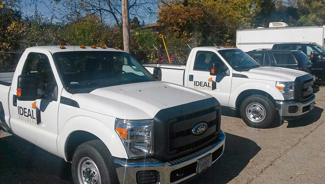 A row of white pickup trucks parked in a parking lot, displaying custom fleet graphics.