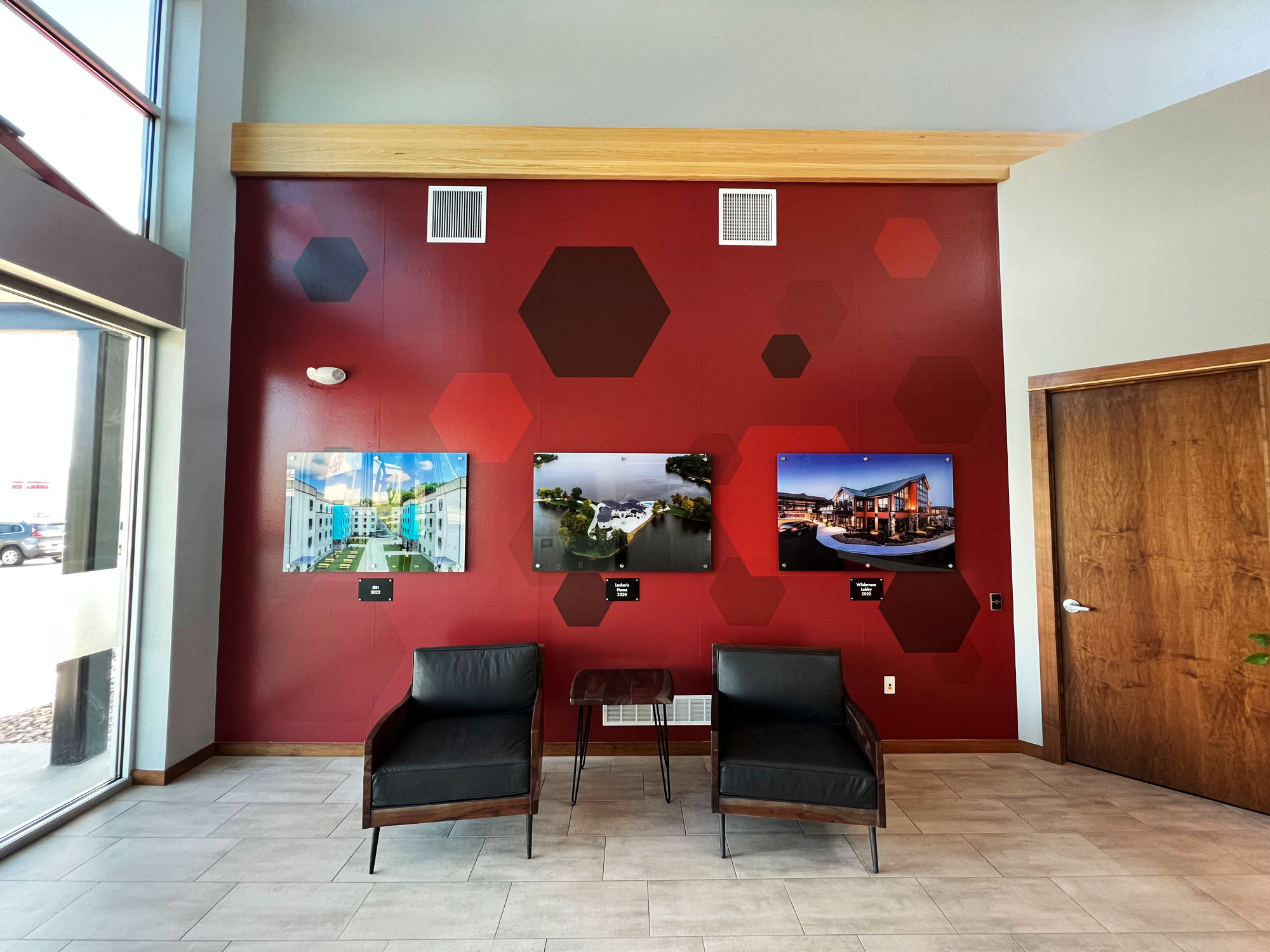 Environmental Graphics for HBI lobby wall featuring a red hexagonal pattern backdrop with mounted architectural photo panels and modern seating.