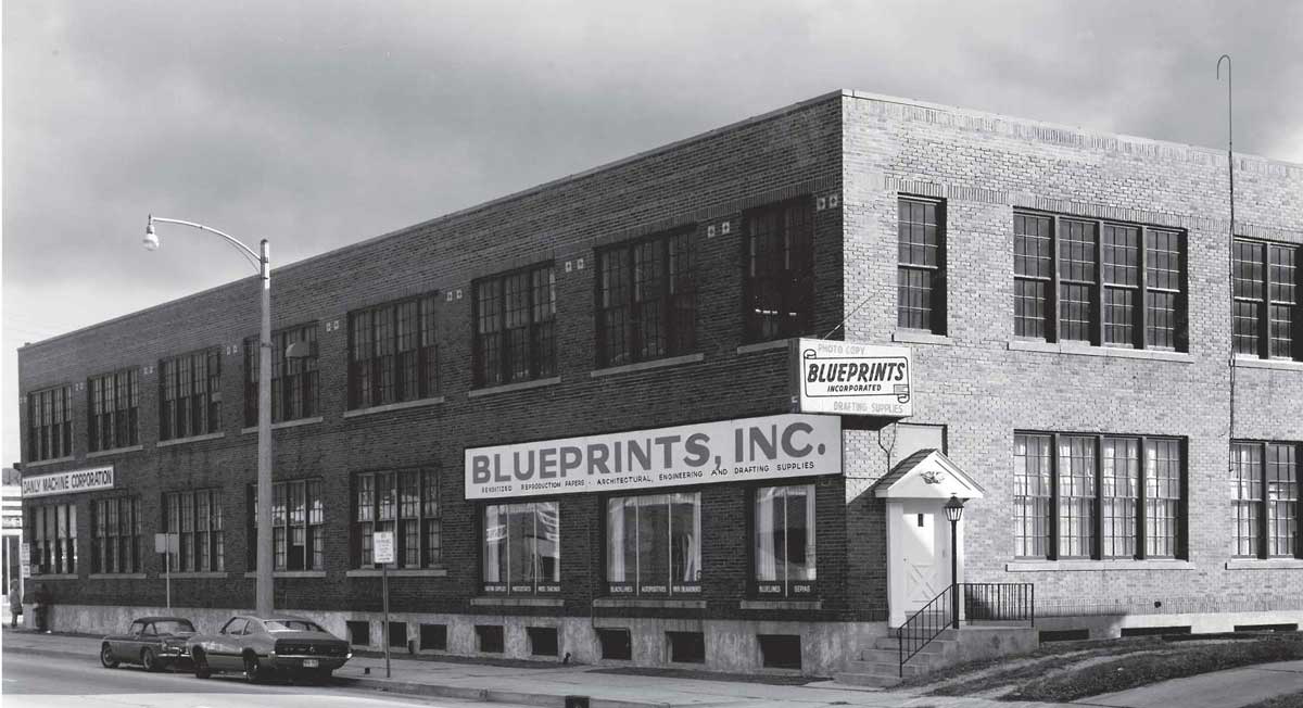 Black and white photo of large corner brick building.