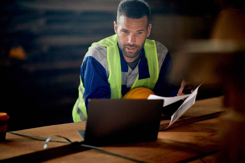 Man wearing a safety vest working on a laptop.