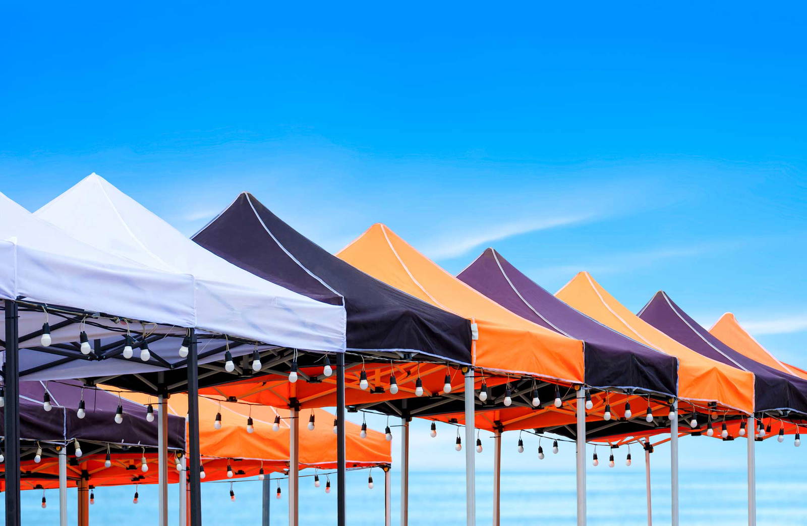 Line of event tents in front of a bright blue sky.