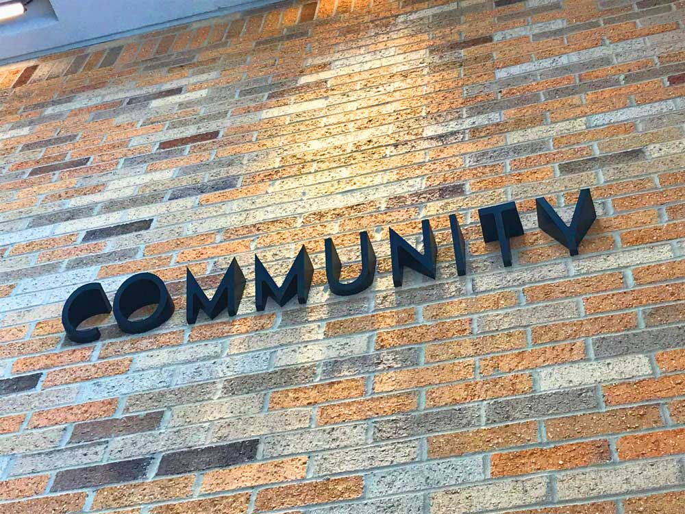 Dark lettering signage on a multi-colored brick wall reading "COMMUNITY".