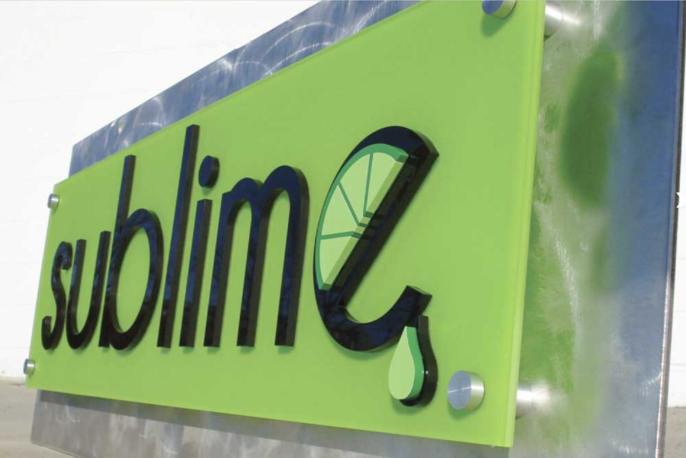 Green lettering signage in black reading "sublime" on a green background, affixed to a slab of metal.