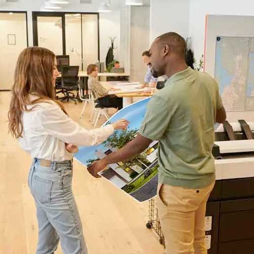 Two coworkers talking next to a printer.