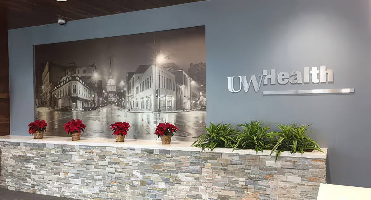 A multicolored brick plantar box with flowers and greenery, displayed in front of a UW Health wall signage.