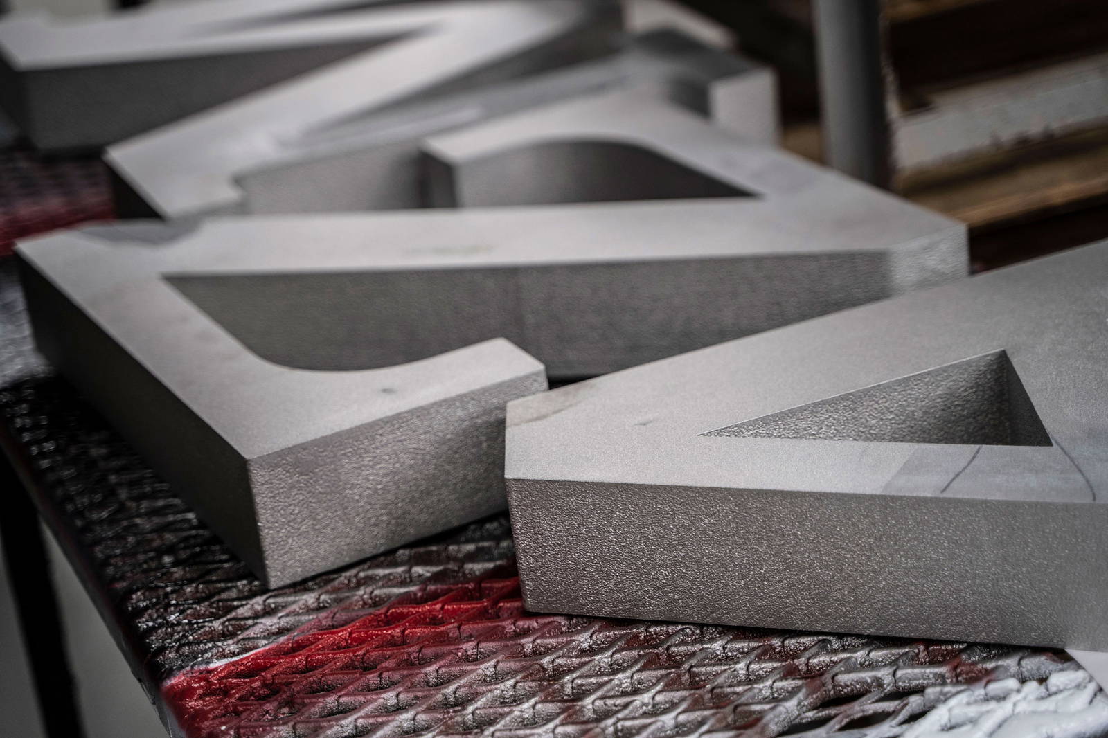 Close-up of large, industrial flat cut metal letters resting on a textured work surface, showcasing their thickness, brushed finish, and clean edges.