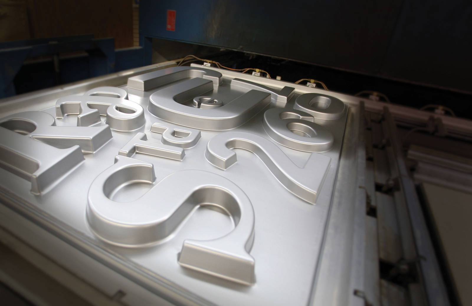 Close-up view of injection-molded metal letters and numbers cooling on a mold tray, showcasing their smooth, three-dimensional shapes and metallic finish in a manufacturing setting.