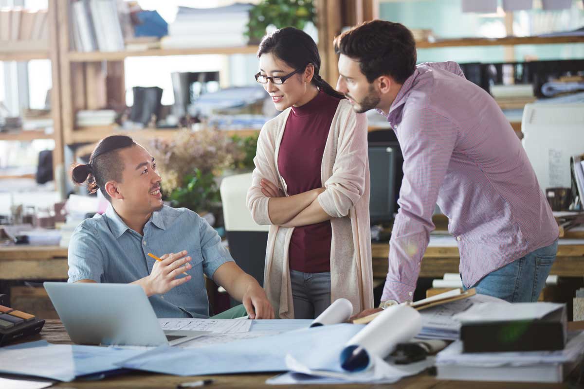 Coworkers, two men and one woman, are working at a laptop together in an office space.