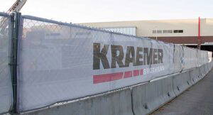 Mesh white construction banner hanging on a chain-link fence,