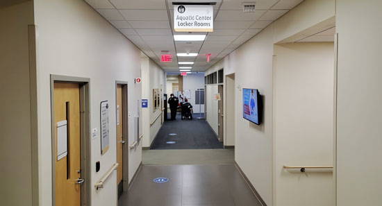 A view down a hallway at a hospital of three people, two are standing and one is in a wheelchair.