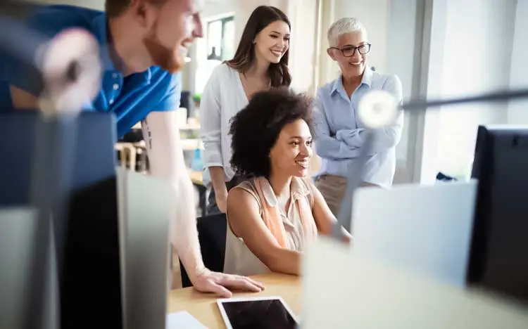 Print Tracking image showing a diverse business team gathered around a computer screen, reviewing printing reports and discussing workflow efficiency.