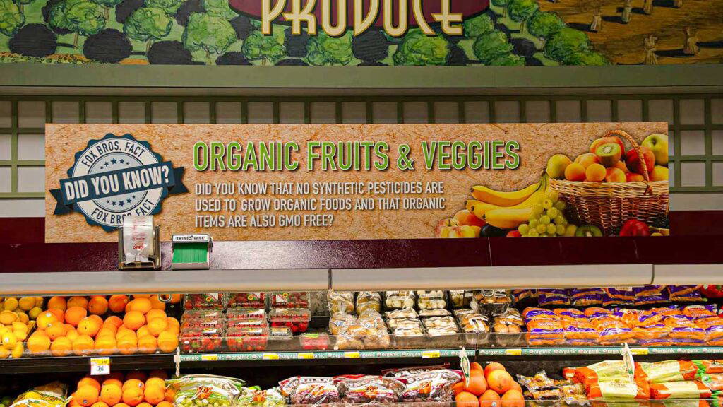 Custom grocery store signage above a produce cooler.