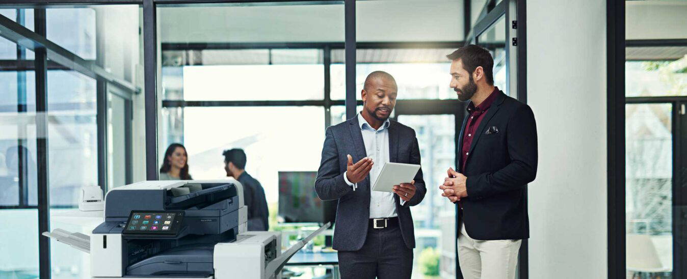 Two office staff meeting near a Xerox printer.