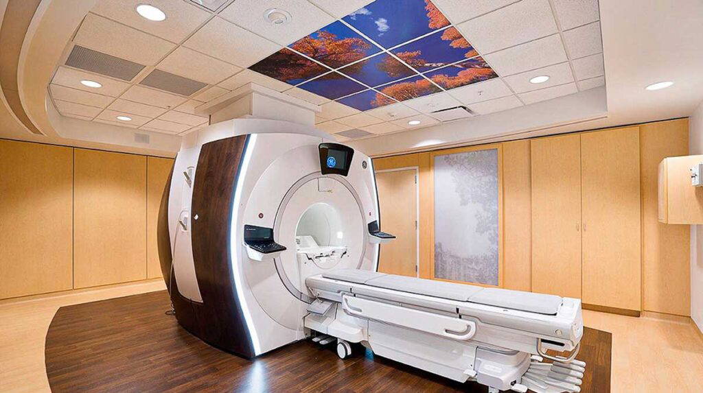 MRI machine in a well lit room, displaying ceiling graphics above the machine for patients to gaze at while receiving their treatments.