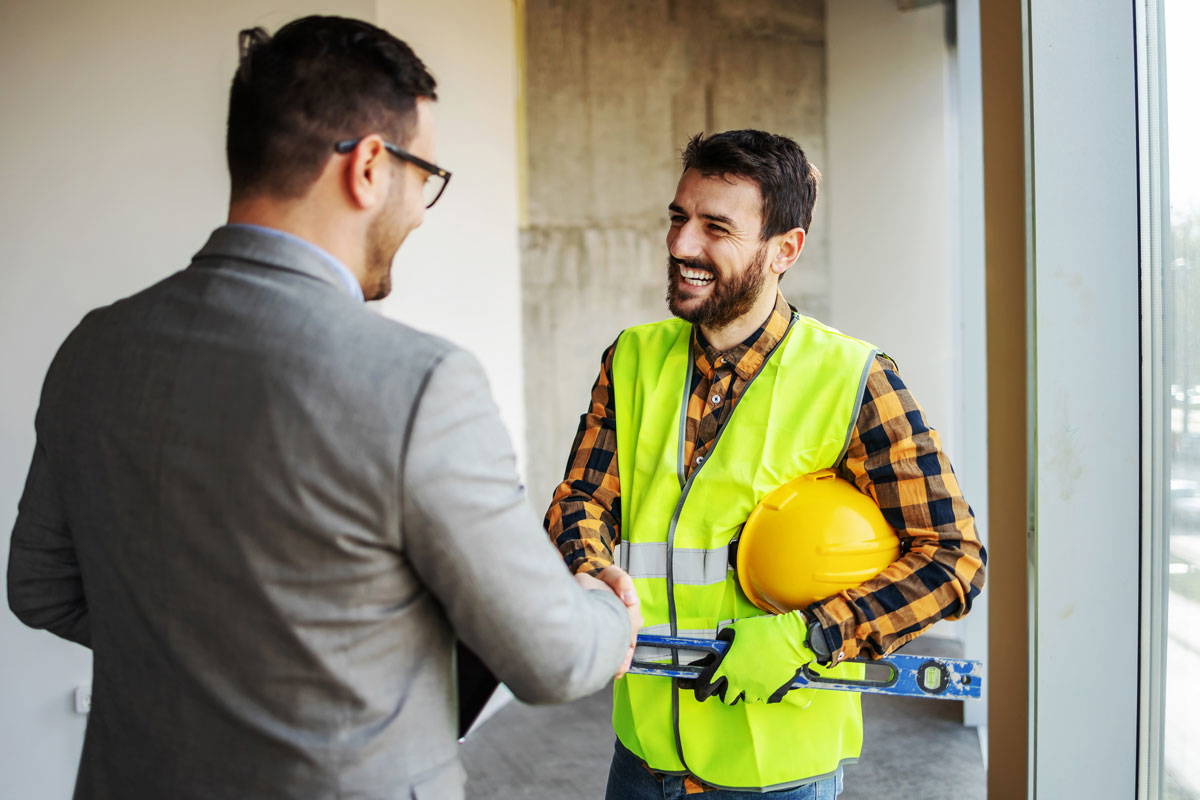 A man in a gray suit shaking hands with a man in a flannel and safety vest.