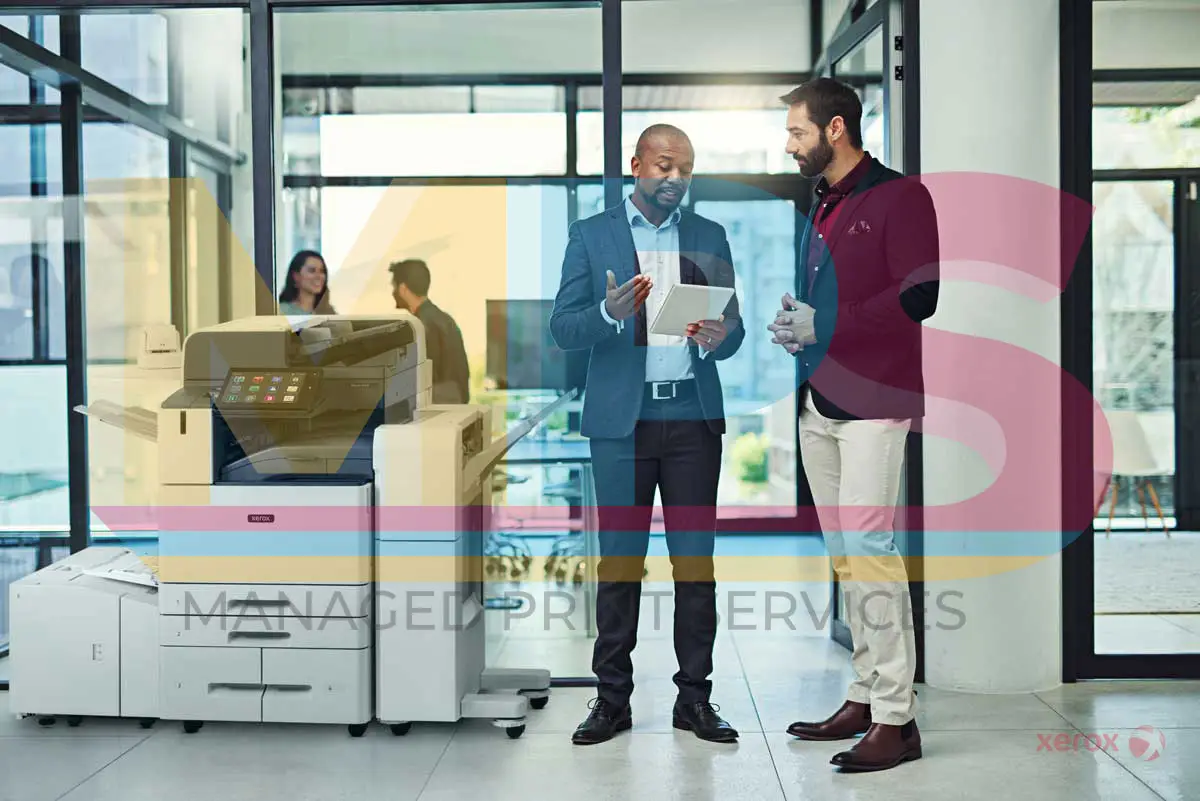 Xerox Lifestyle Photo of two professionals discussing Managed Print Services in a modern office setting, featuring a Xerox multifunction printer in the foreground.