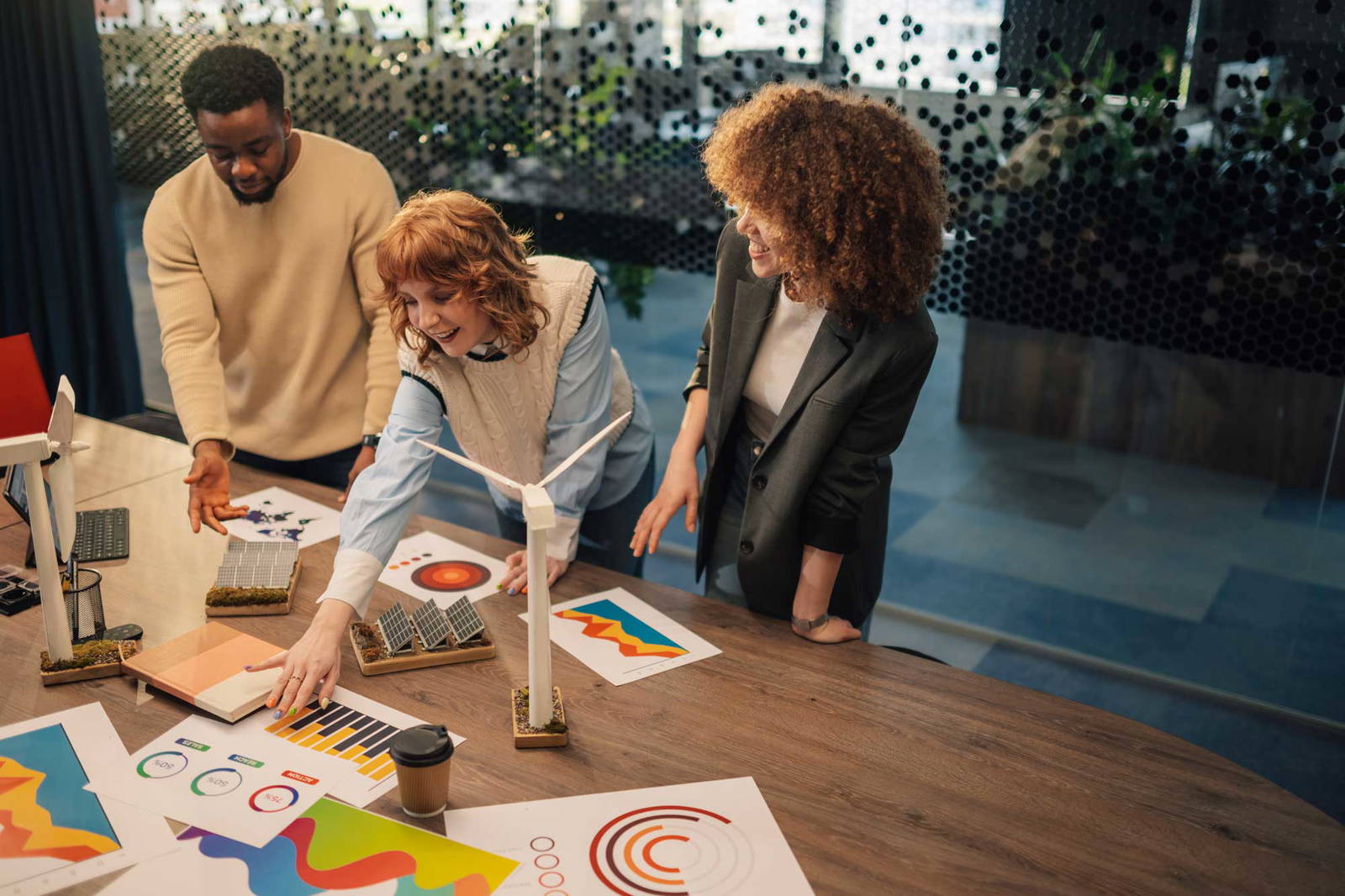 Graphics & Signage Menu showcasing a creative team collaborating around a table with printed charts, solar models, wind turbine models, and branding materials.