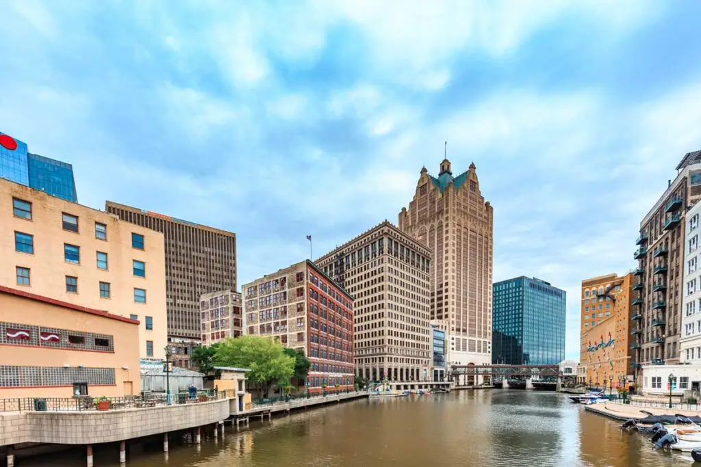 Downtown Milwaukee skyline view featuring the Milwaukee River, historic architecture, and iconic high-rise buildings on a partly cloudy day.