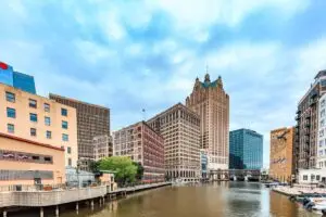 Downtown Milwaukee skyline view featuring the Milwaukee River, historic architecture, and iconic high-rise buildings on a partly cloudy day.