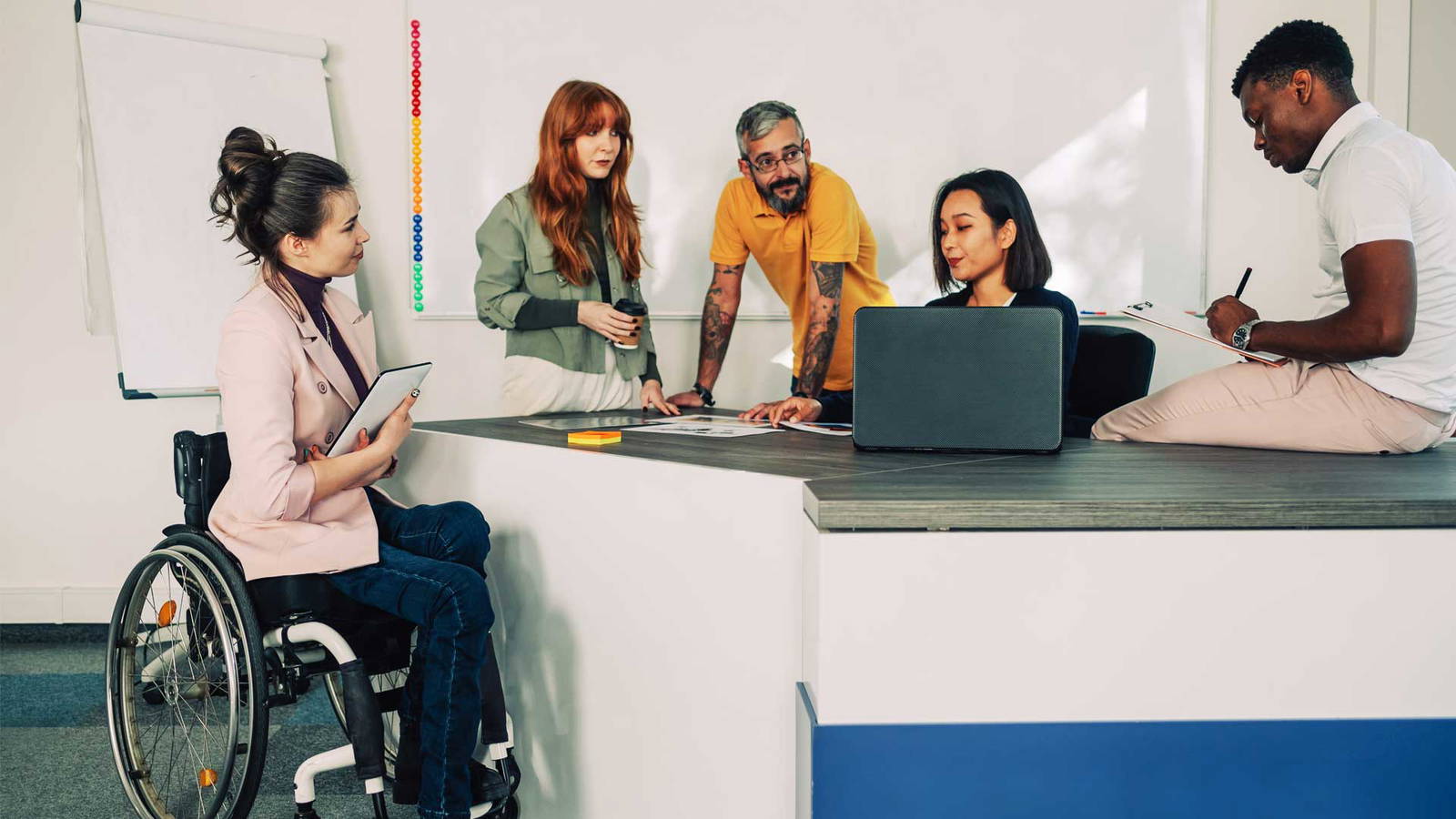 Five coworkers working around a desk.