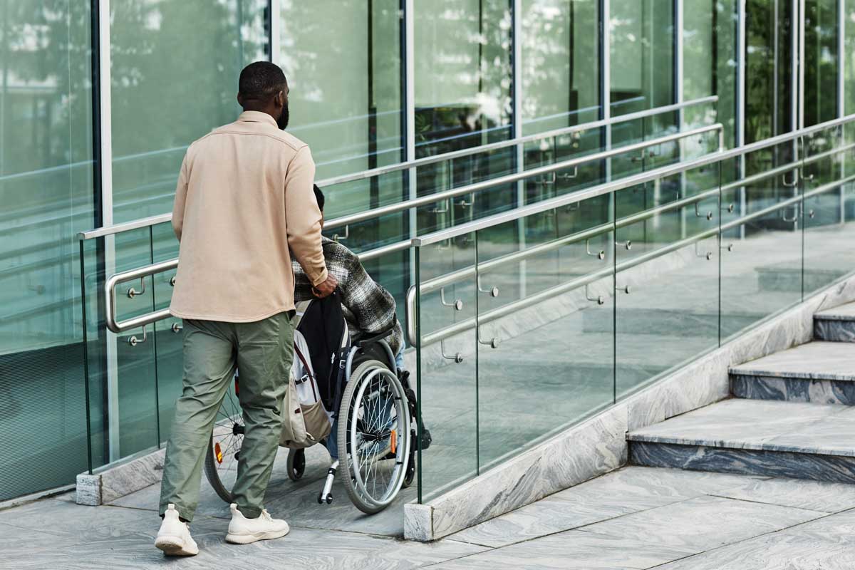 Person assisting a person in a wheelchair up a ramp.