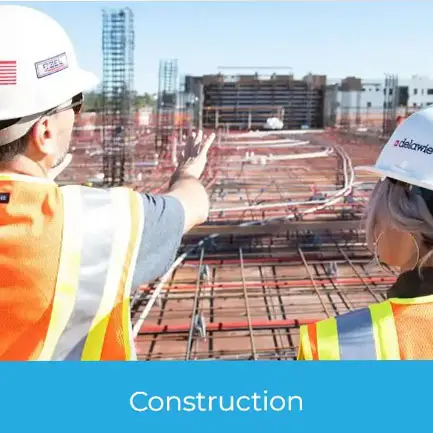 Construction Promotional Products image showing two workers in safety vests and hard hats reviewing site progress on a large active construction project.