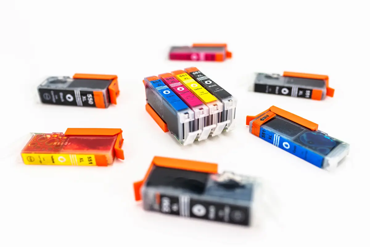 Printer Ink Cartridges arranged on a white surface, showing a variety of colors including cyan, magenta, yellow, and black with protective orange caps.