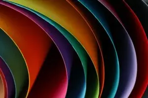Colorful paper curves in vibrant shades of red, green, orange, and blue create a layered, flowing background with deep shadows and rich texture.