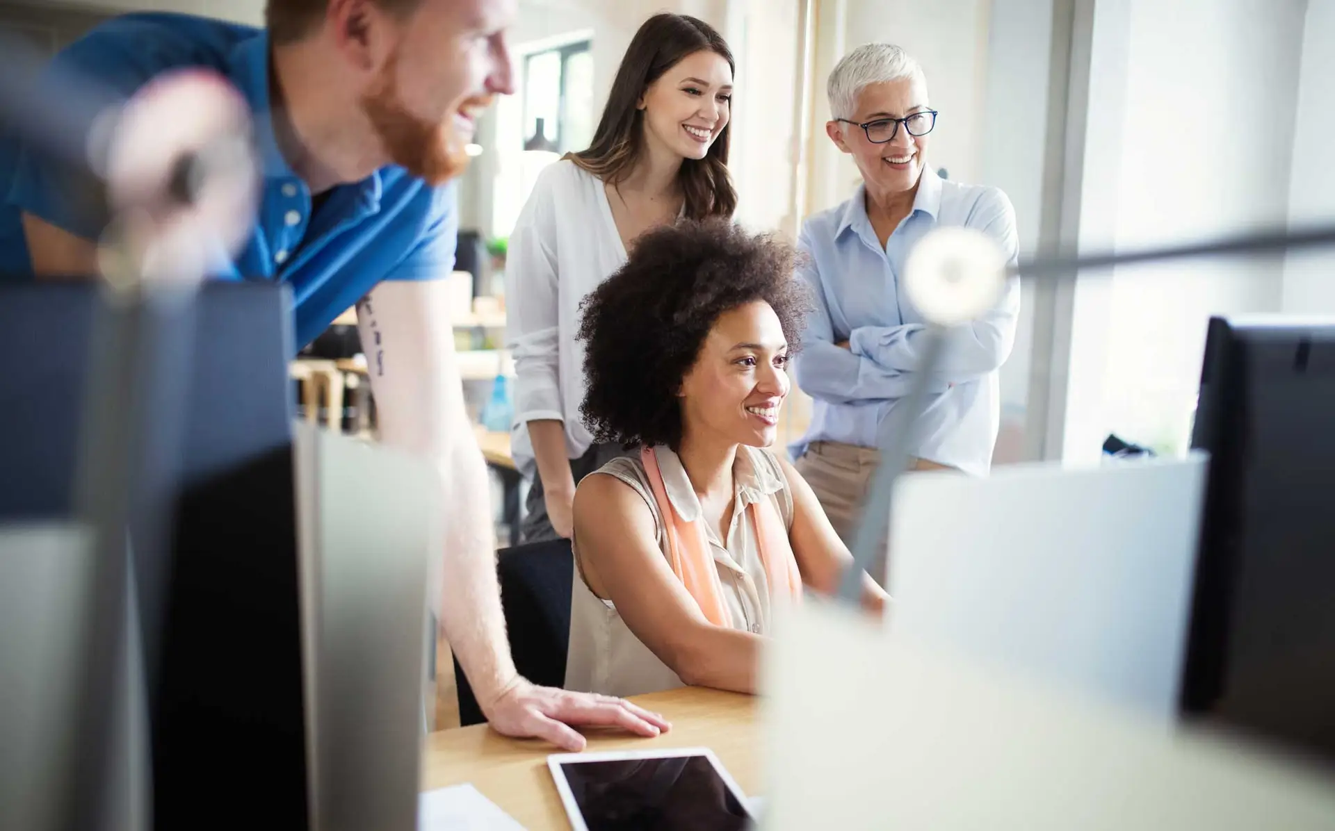 Print Tracking image showing a diverse business team gathered around a computer screen, reviewing printing reports and discussing workflow efficiency.