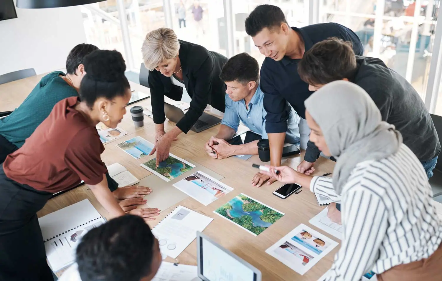 Collaboration in an Office Setting with a diverse team of professionals gathered around a table, reviewing maps and documents during a productive planning session.