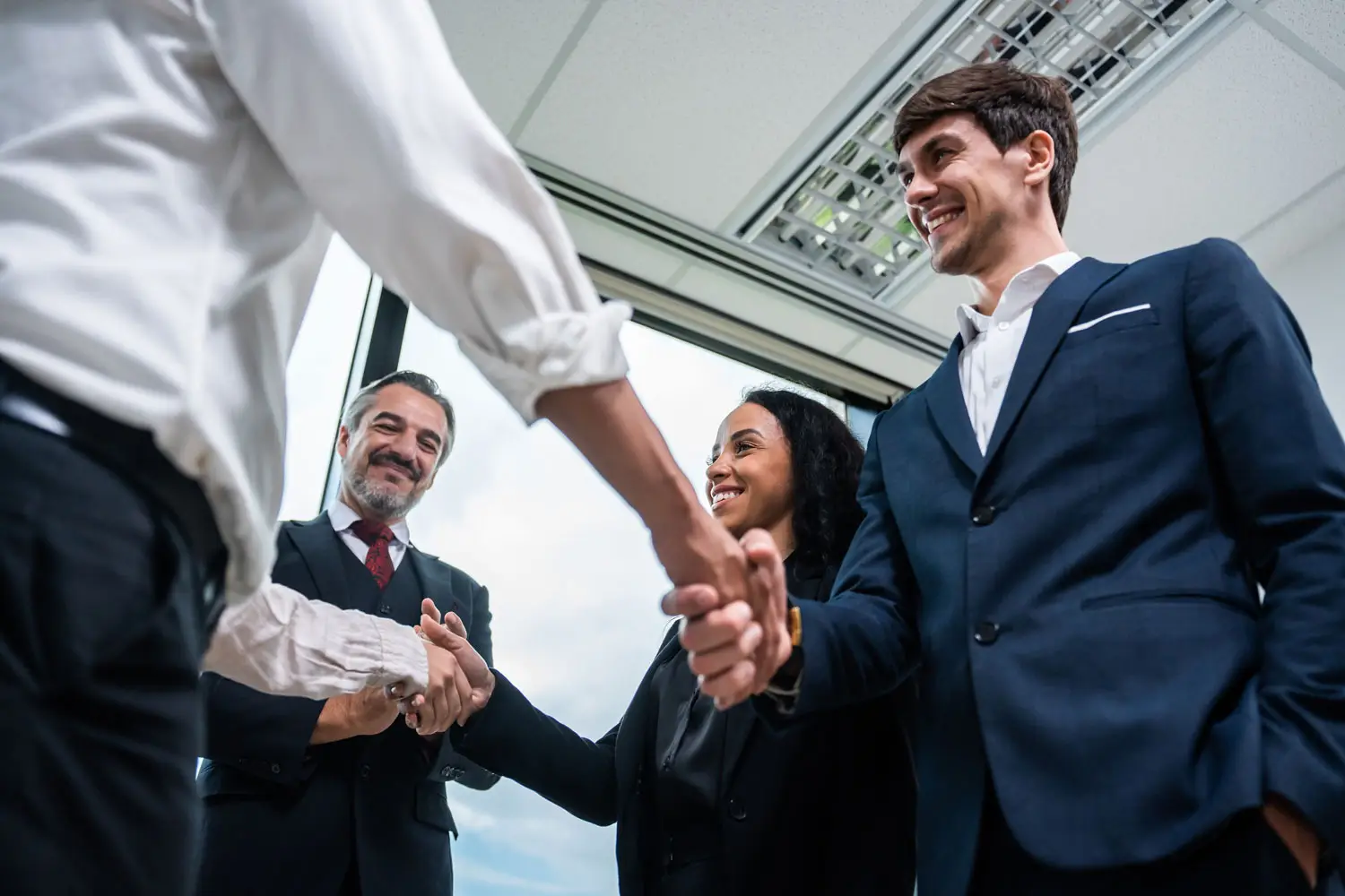 Respect in Business demonstrated through a group of diverse professionals exchanging firm handshakes and smiling during a successful meeting in a corporate office.