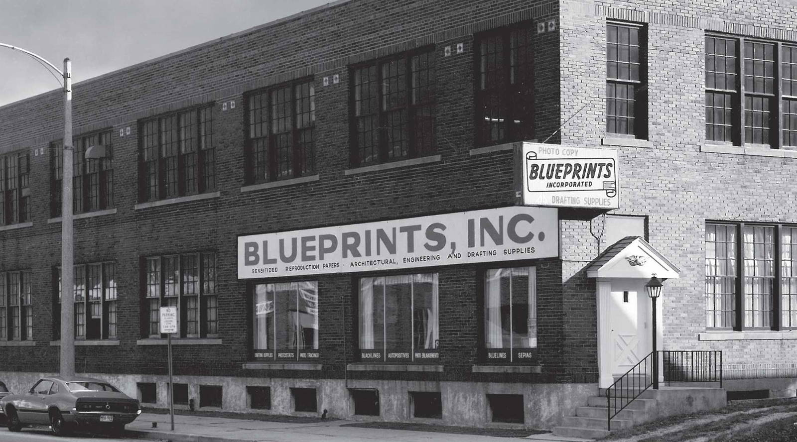 Black and white photo of large corner brick building.