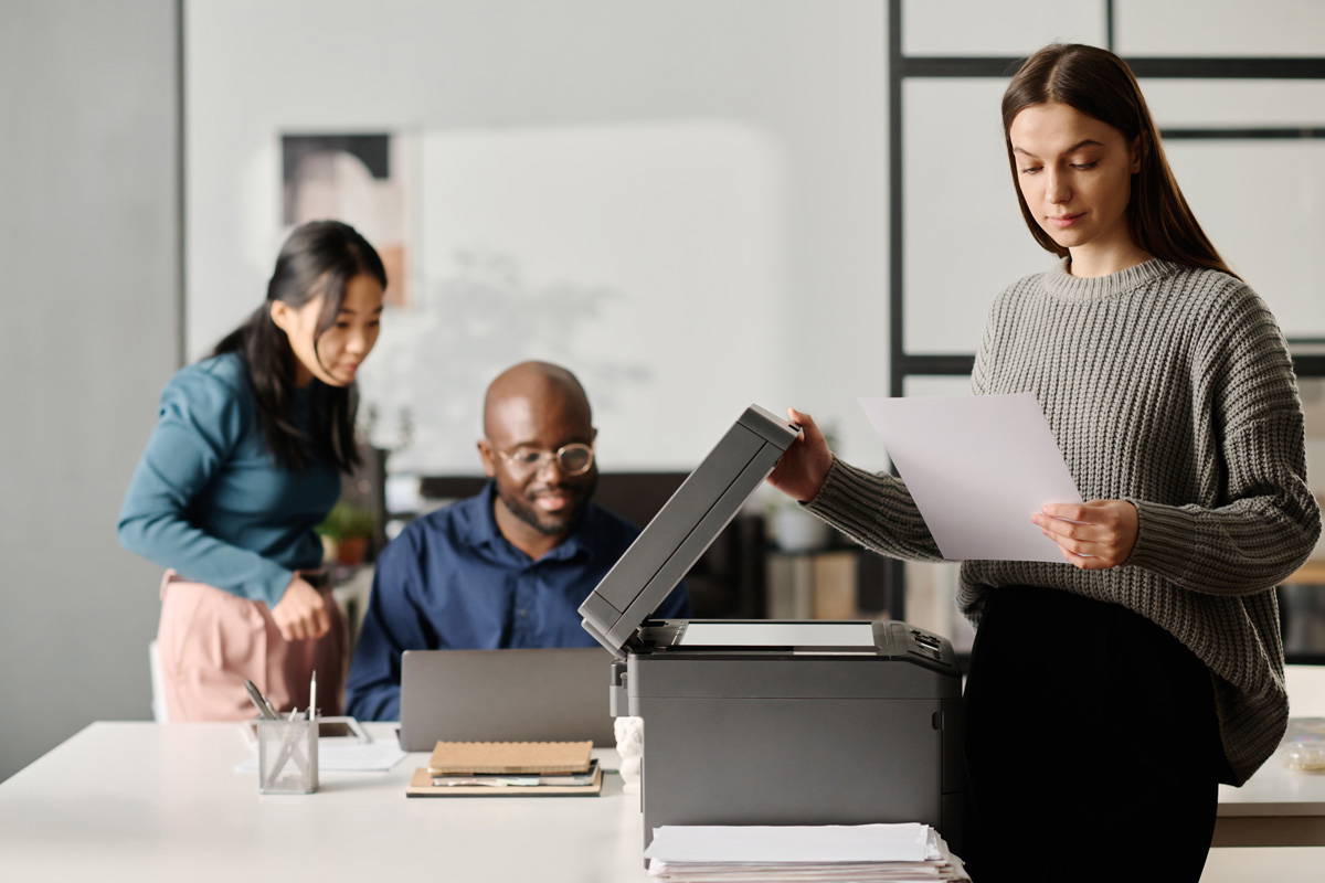 P-R-A-C-T-I-C-E Core Values with BPI Color: Accountability 4 3 office coworkers working around a printer.
