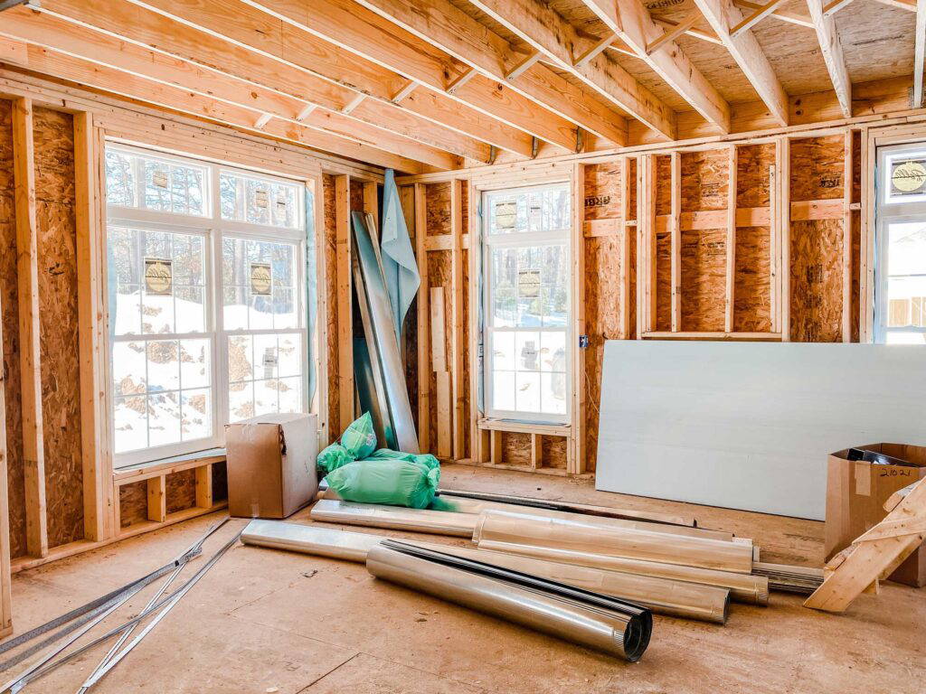 Liberty Remodeling & Construction 2 Interior view of a residential construction site showing exposed wooden framing, new window installations, insulation materials, and construction supplies on the floor.