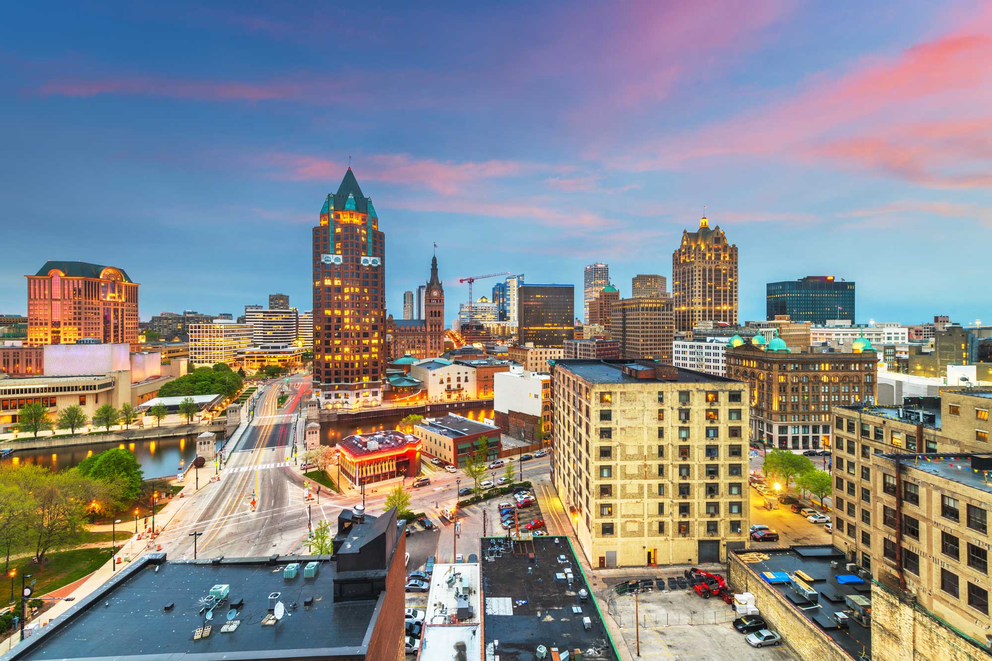 skyline at dusk showcasing downtown buildings, bridges, and city lights beneath a vibrant pink and blue sky.