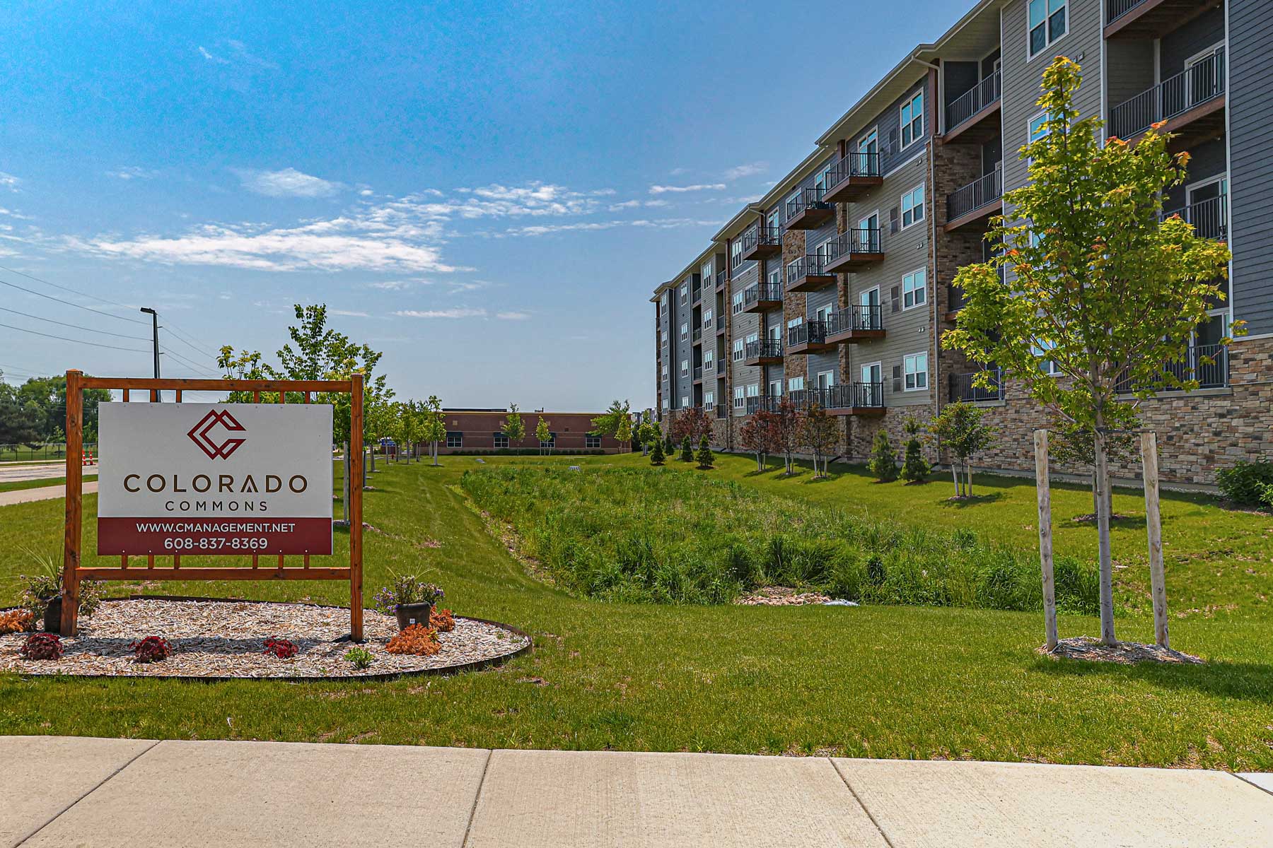 Portfolio for Colorado Commons exterior signage and apartment building shown on a sunny day, highlighting landscaping and branding for the residential complex.