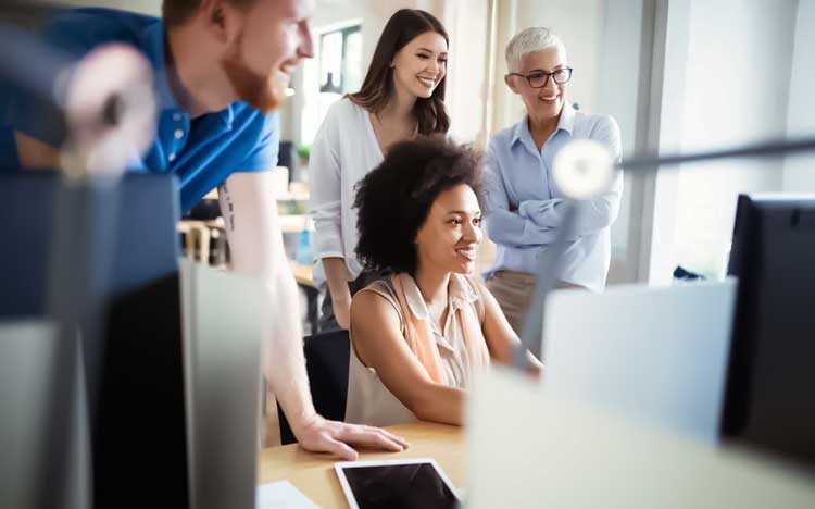 Print Tracking image showing a diverse business team gathered around a computer screen, reviewing printing reports and discussing workflow efficiency.