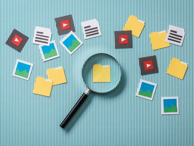 File Asset Management concept image showing a magnifying glass over a folder icon, surrounded by icons representing media files and documents.
