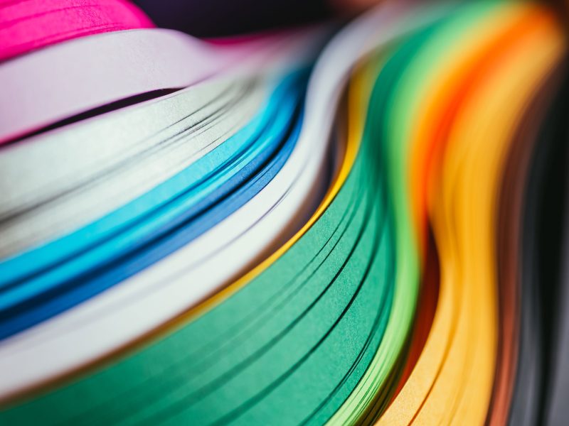 Colorful paper stacked in a smooth wave pattern, featuring vibrant hues like pink, blue, green, yellow, and orange in a high-resolution close-up.